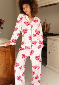 Wit pyjama set met roze hartpatronen, met lange mouwen, een knopenfront en bijpassende broek met een elastische tailleband.