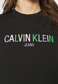 Černé bavlněné tričko s vícebarevným vyšívaným nápisem "CALVIN KLEIN JEANS" v moderním písmu. Design s kulatým výstřihem.