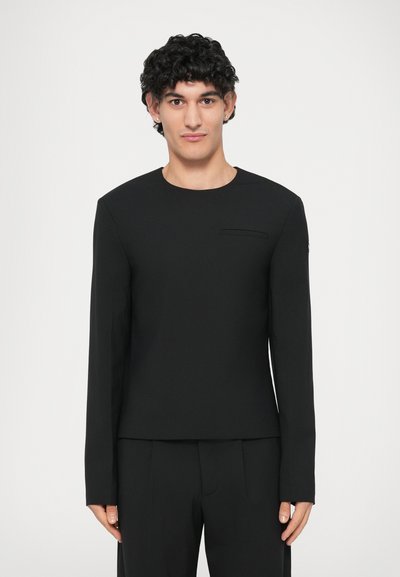 Tricou lung cu mânecă negru, cu guler tip crew, având un mic buzunar frontal, realizat dintr-un material neted cu o textură subtilă și o siluetă ajustată.