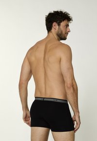 Czarne bokserki z szarą gumką, wykonane z miękkiego materiału. Krój dopasowany, ukazujący plecy i boczny profil osoby noszącej.
