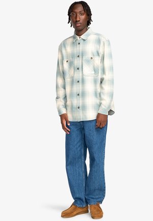 Világoskék és fehér kockás flanel ing, két mellzsebbel, kék farmernadrággal és barna, slip-on cipőkkel párosítva.