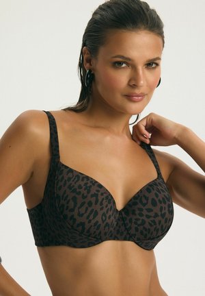 Žena s mokrými vlasmi, ktorá má na sebe čierno-hnedú podprsenku s leopardím vzorom, dotýka sa krku, čelí dopredu s neutrálnym pozadím.