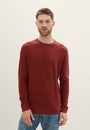 Suéter rojo de canalé con mangas largas y escote redondo, combinado con vaqueros azules. La textura es de punto, ofreciendo una apariencia suave.