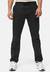 Black linen pants with a drawstring waist, straight leg design, and side pockets, paired with white athletic shoes.