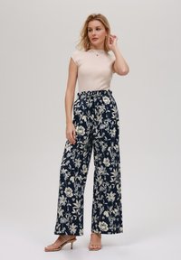 Marineblå blomsterbukser med vid benfacon har en høy elastisk midje og hvite og kremfargede blomstermønstre, kombinert med en tettsittende lys beige topp.