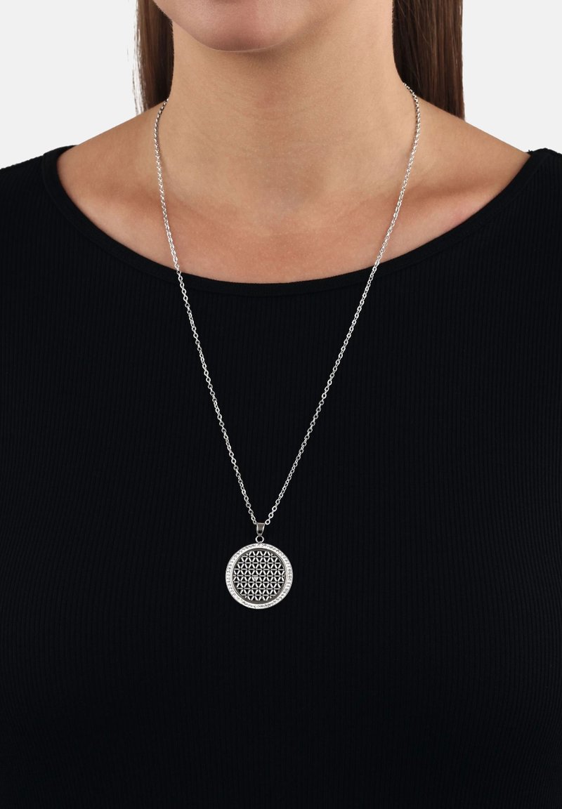 Collana con pendente argento con motivo geometrico intagliato, attaccata a una catena sottile, indossata sopra un top nero a coste.