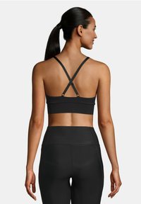 Sujeción deportiva negra con tirantes entrelazados y una textura suave, combinada con leggings negros de cintura alta. Diseño sencillo, con hardware mínimo.