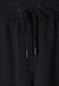 Black drawstring pants with a textured fabric, featuring a smocked waistband and black cord ties with metal tips.
