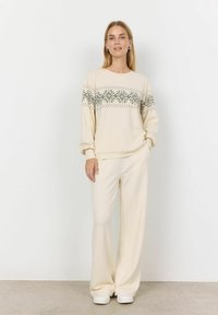 Crème gebreid sweatshirt met zwart sneeuwvlokpatroon over de borst, gecombineerd met crème wijde broek en witte sneakers. Zachte textuur.