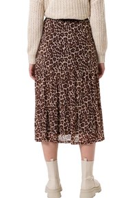 Personne portant une jupe midi à volants imprimée léopard, un pull en maille crème et des bottes épaisses crème, vue de dos sur fond blanc.