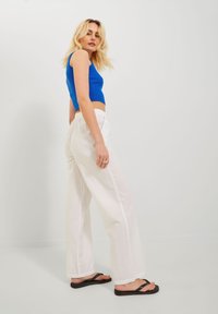 Blue cropped tank top, white linen wide-leg pants, black flip-flops. Model stands sideways against a plain white background.