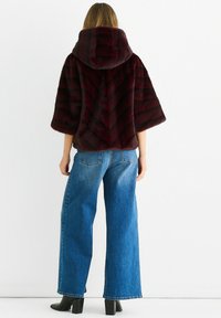 Burgundy faux fur jacket with a chevron pattern and a large hood, paired with high-waisted blue wide-leg jeans and black ankle boots.
