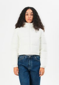 Witte, korte pufferjack met rits en textuurpanelen. Gecombineerd met blauwe high-waisted jeans voor een casual uitstraling.