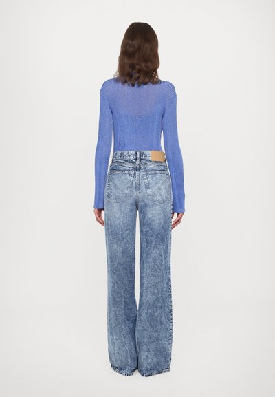 Blue ribbed long-sleeve top paired with high-waisted, wide-leg light-wash denim jeans featuring a tan leather patch on the back.