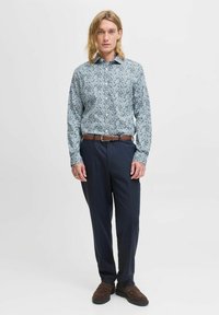 Camicetta a maniche lunghe con motivo blu e bianco, abbinata a pantaloni scuri e scarpe marroni. Presenta un colletto a punta e una chiusura con bottoni.