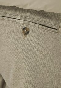 Pantaloni di tessuto grigio con un motivo a spina di pesce, dotati di un bottone marrone e di una piccola tasca sul retro. Superficie testurizzata.