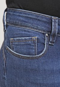Dark blue denim jeans with a high waist, featuring a small back pocket and contrasting stitching. Texture is smooth, with a classic fit.