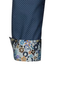 Tessuto blu navy con pois bianchi, dotato di un motivo floreale in blu, arancione e nero sul polsino. Lunghezza delle maniche regolata visibile.