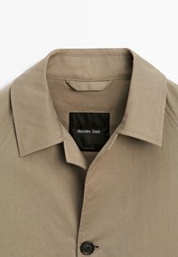 Camicia beige con collo e bottoni, con bottone nero visibile e etichetta interna nera con la scritta "Massimo Dutti".
