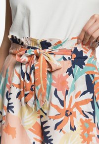Shorts en tissu floral à motifs avec une large ceinture, un nœud noué et des couleurs vives incluant l'orange, le bleu sarcelle et le bleu marine.