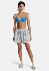 Brassière bleue texturée avec fines bretelles, associée à un short rayé clair avec une ceinture élastique et un accent argenté. Baskets blanches.