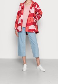 Vandtæt regnjakke med røde og pink striber, pink v-hals sweater, lyseblå denim culottes og hvide sneakers. Afslappet pasform og design.