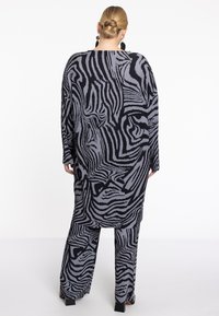 Zwart en grijs oversized outfit met een gestreept patroon, geribde textuur en brede mouwen, tegen een witte achtergrond.