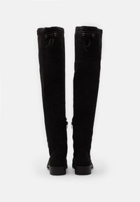 Black suede over-the-knee boots with a fitted silhouette, featuring lace-up accents at the top and side zippers. Flat rubber sole.