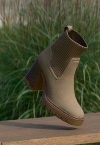 Bottine beige avec une chaînette élastique à côtes et un large talon. Présente une semelle texturée pour plus d'adhérence et une finition lisse et mate.