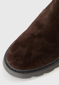 Botte en daim marron à bout rond, avec un dessus texturé et une semelle en caoutchouc noir, démontrant un design épuré et simple.