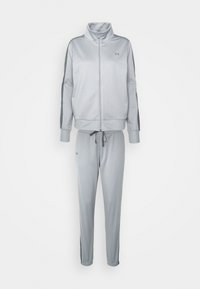 Veste de survêtement zippée gris clair avec pantalons assortis à cordon, bandes latérales gris foncé et petits logos sur la poitrine et la cuisse.