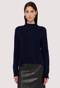 Marinblå stickad tröja med rund halsringning, långa ärmar och ribbade muddar. Texturerat tyg med lös passform, kombinerad med en svart läderkjol.