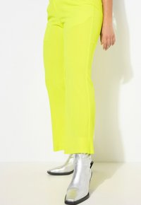 Pantalons droits jaune néon en tissu lisse. Associés à des bottines argentées à bout pointu avec des coutures décoratives.