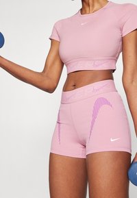 Rosa atletisk crop top och shorts, med ribbade kanter och lila randiga detaljer. Tillverkade av stretchtyg för komfort under träning.