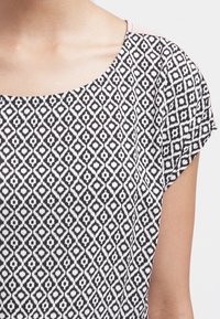 Svart och vit mönstrad topp med diamantformer, korta ärmar och rundad halsringning. Lättviktig tyg med en slät textur.