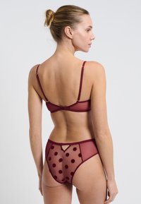 Ensemble de lingerie bordeaux comprenant un soutien-gorge transparent avec des bretelles réglables et une culotte transparente à pois assortie, dotée d'une petite découpe triangulaire.