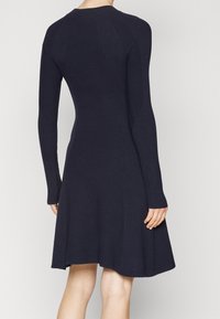 Granatowa dzianinowa sukienka z długimi rękawami, dopasowanym gorsetem i rozszerzanym dołem. Charakteryzuje się pionową, prążkowaną fakturą na ramionach i bokach.