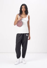 Hvit tanktopp med "SPORTS" grafikk, svarte joggebukser med hvite sidepaneler, og en liten rund rosa veske. Modell med hvite sneakers.