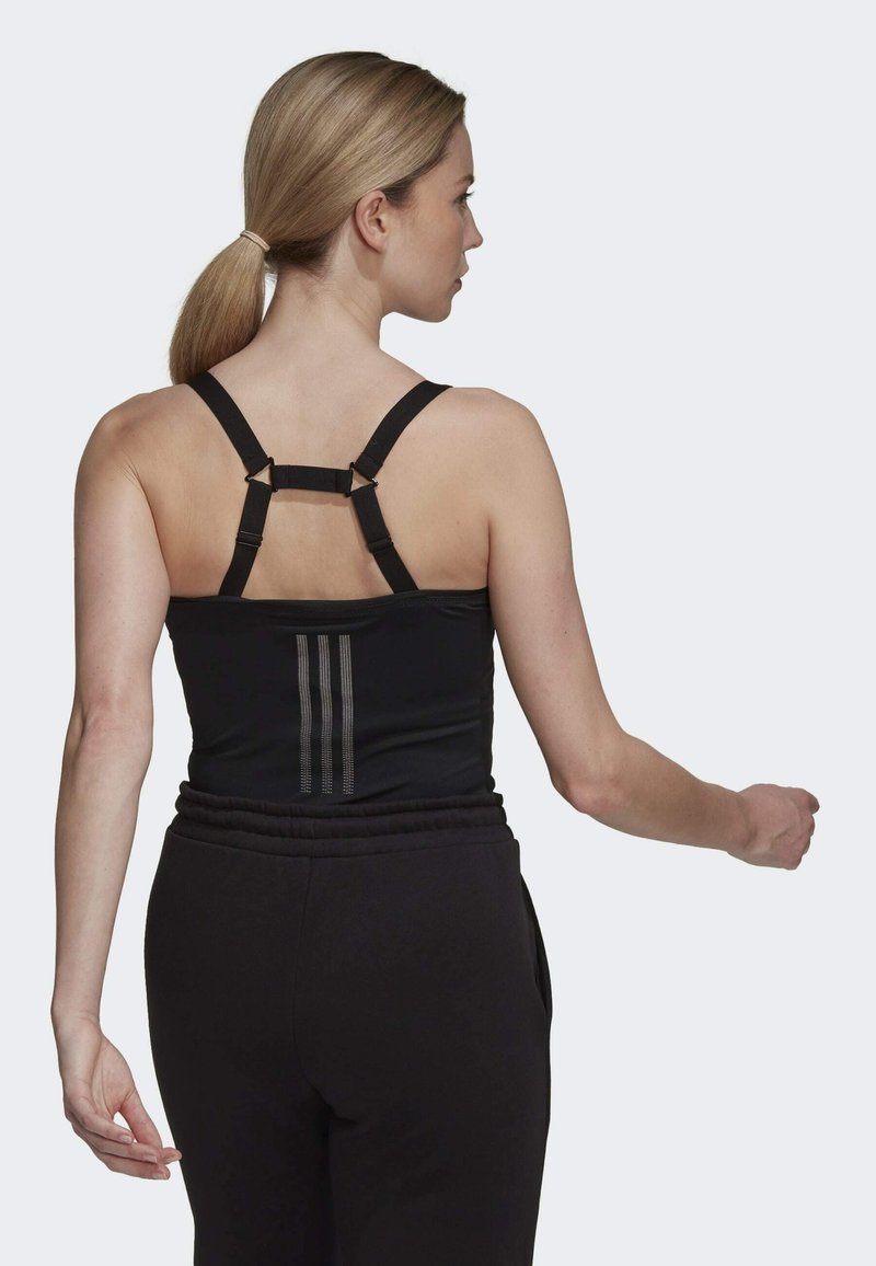 Schwarzes Tanktop mit verstellbaren Trägern, das auf der Rückseite mit einem gestreiften Detail versehen ist, kombiniert mit schwarzen Sporthosen. Glatte Textur.