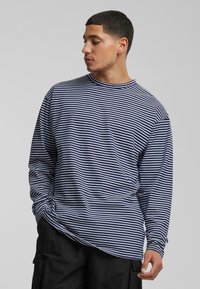 Long-sleeve shirt in navy and white stripes, cotton material, relaxed fit, crew neckline, with side seam detail and dropped shoulder design.