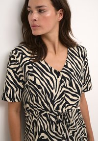 Sukienka w leopardzie w kolorze kremowym i czarnym, z dekoltem w serek, krótkimi rękawami, guzikami oraz przewiązanym w pasie detalem. Teksturowany materiał.