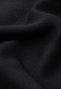 Czarna tkanina o fakturowanym splocie, opadająca w miękkie fałdy. Powierzchnia wygląda na matową i jednolitą, ukazując subtelny, równomierny kolor.