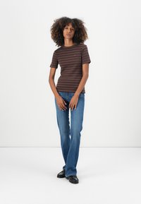 Gestreiftes T-Shirt in Braun und Lila mit kurzen Ärmeln, kombiniert mit blauen Jeans und schwarzen Schuhen. Einfaches Design mit Rundhalsausschnitt.
