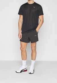 Svart sporttröja med korta ärmar, matchad med mörka shorts. Skorna är vita sneakers med röda och svarta detaljer.