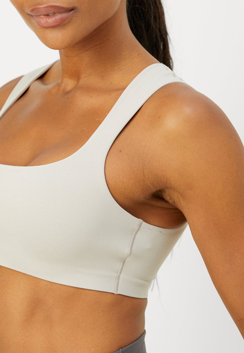 Lichtgrijze sportbeha met brede bandjes, een gladde textuur en een aangesloten ontwerp. Bevat platte naden voor comfort en een minimalistische stijl.