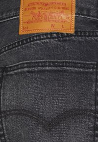 Takapuoli mustista farkuista, jossa on ruskea nahkaonnelma, jossa on kaksi hevosta ja teksti "Aito Laatukangas."