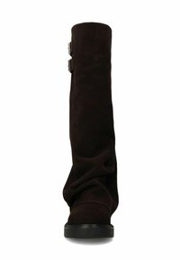 Hoge zwarte nubucklaarzen met een lage platte zool en twee zijgespen, weergegeven vanaf de voorkant op een witte achtergrond.