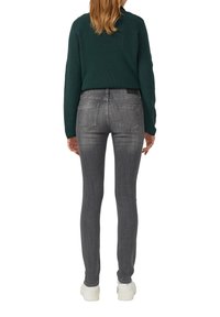 Jeans skinny en denim gris avec une texture lisse, poches arrière et un design minimaliste, associés à un pull en tricot vert foncé et des baskets blanches.