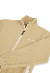 Μπεζ μπουφάν Sherpa fleece με πλήρες φερμουάρ μπροστά, ψηλό γιακά, ελαστικά μανίκια και λογότυπο O'Neill στο αριστερό στήθος.