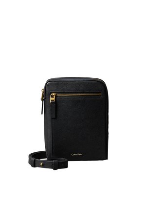 Sac bandoulière texturé noir Calvin Klein avec poche à fermeture éclair dorée et sangle réglable sur fond blanc.